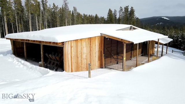 snow covered structure featuring a view of trees and an outdoor structure