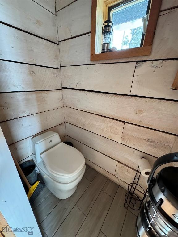 bathroom with toilet, wooden walls, and wood finished floors