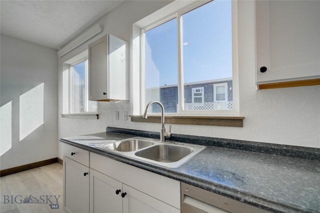 kitchen featuring dark countertops, dishwasher, white cabinetry, and a sink