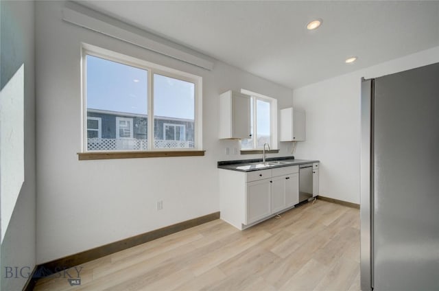 kitchen featuring stainless steel appliances, light wood-style floors, white cabinetry, a sink, and baseboards