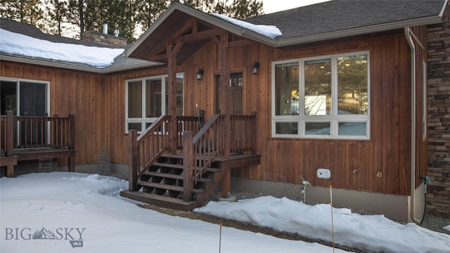 snow covered property entrance featuring a shingled roof and a chimney