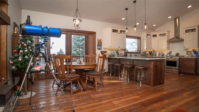 kitchen with stainless steel range with electric stovetop, wall chimney exhaust hood, a breakfast bar area, and dark wood finished floors