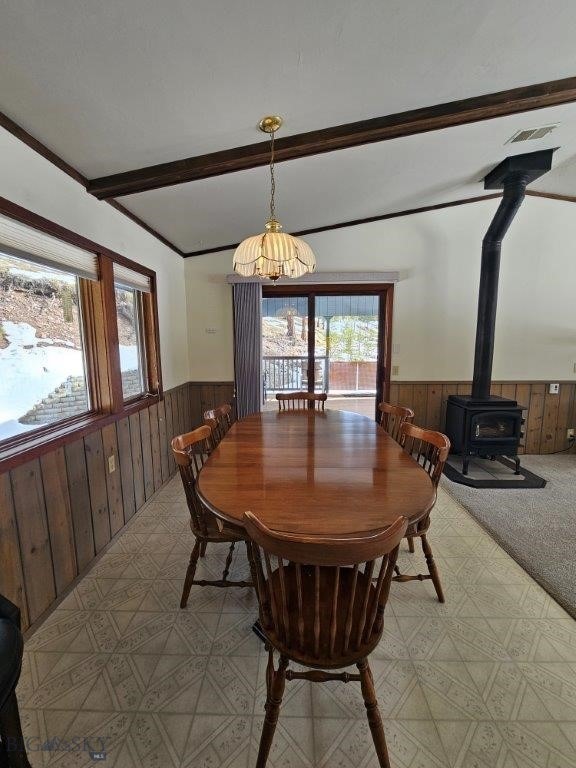 dining room with a wainscoted wall, beamed ceiling, a wood stove, and wooden walls