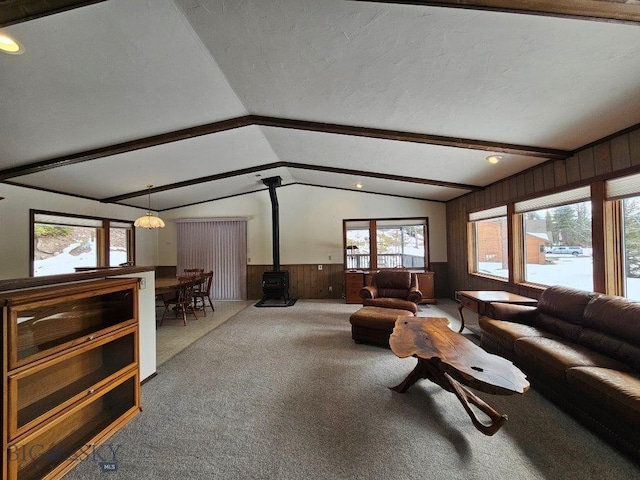 carpeted living room featuring vaulted ceiling with beams, a wood stove, wainscoting, wood walls, and a textured ceiling