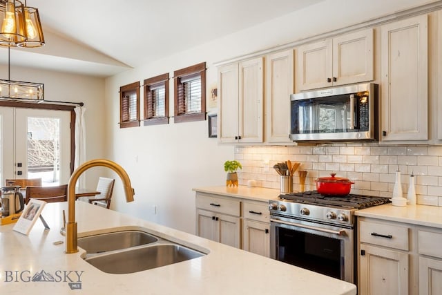 kitchen with lofted ceiling, a sink, stainless steel appliances, light countertops, and backsplash