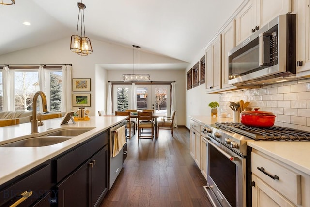 kitchen with appliances with stainless steel finishes, dark wood-type flooring, vaulted ceiling, light countertops, and a sink