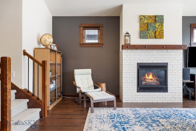 living area featuring a brick fireplace, stairway, and wood finished floors