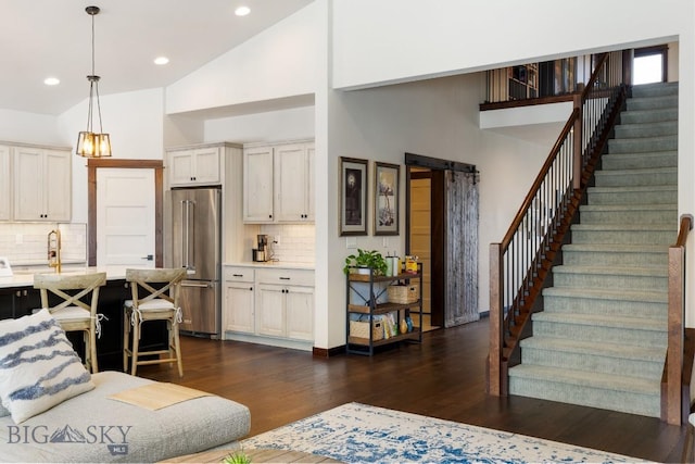 living room with dark wood-type flooring, stairs, high vaulted ceiling, and a barn door