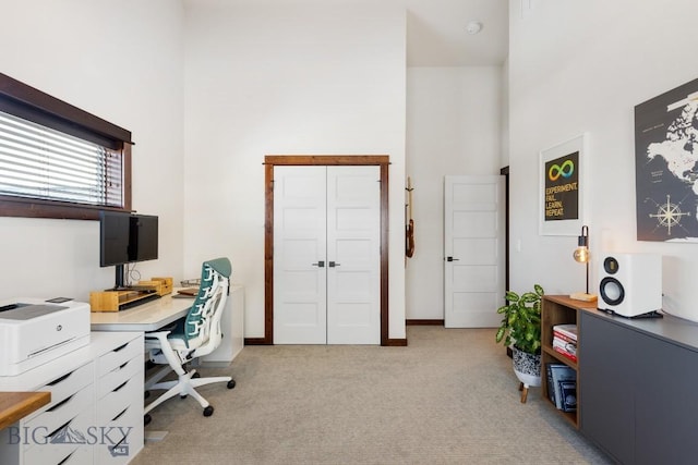 office space featuring baseboards, a towering ceiling, and light colored carpet