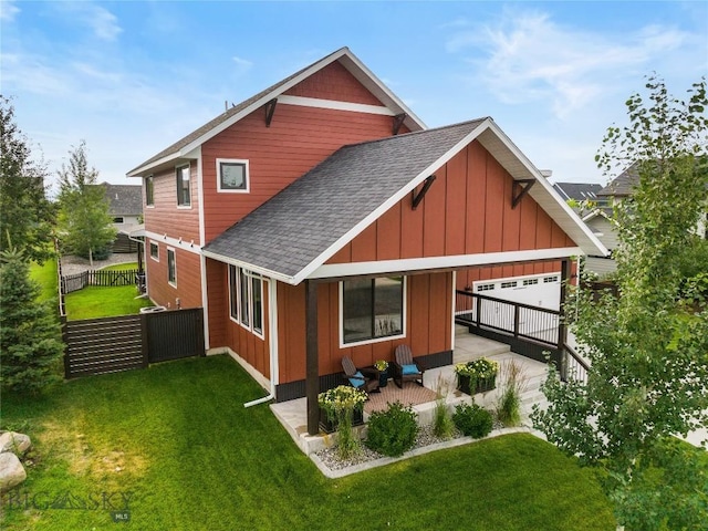 rear view of property with roof with shingles, a lawn, board and batten siding, and fence