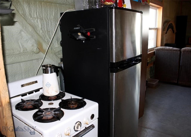 kitchen with white range with gas stovetop, concrete flooring, and freestanding refrigerator