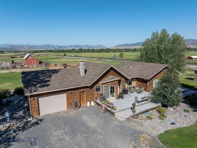view of front facade featuring roof with shingles, an attached garage, a deck with mountain view, gravel driveway, and a rural view