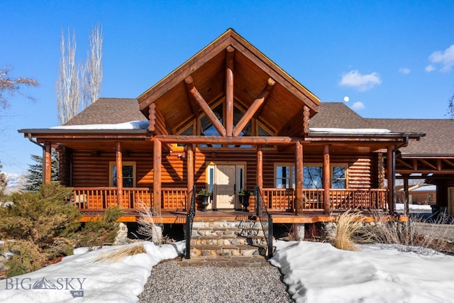 log-style house with covered porch, log exterior, and a shingled roof