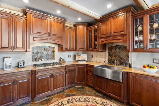 kitchen with light stone counters, stone tile flooring, stainless steel gas cooktop, and a sink