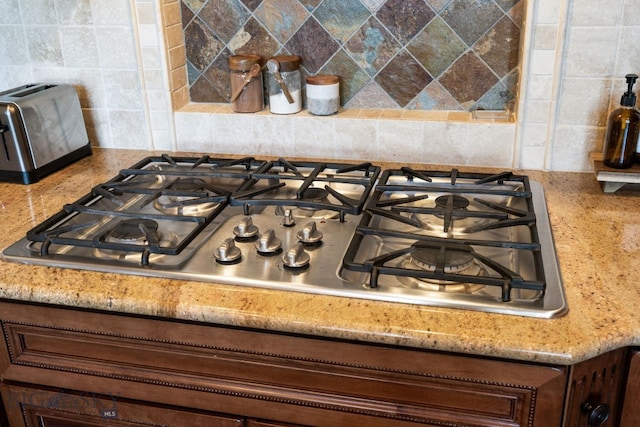 interior details with tasteful backsplash, a toaster, stainless steel gas cooktop, and light stone countertops