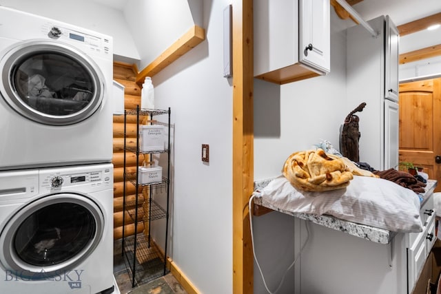 clothes washing area featuring stacked washer / drying machine, stone finish floor, cabinet space, and baseboards