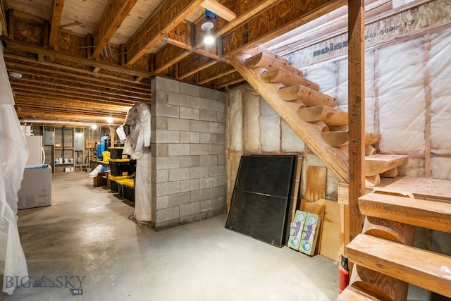 unfinished below grade area featuring white refrigerator, concrete block wall, and electric panel