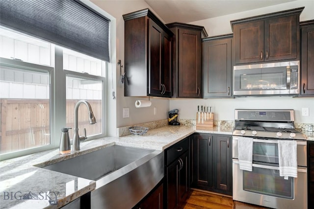 kitchen featuring a sink, light stone counters, wood finished floors, stainless steel appliances, and dark brown cabinets