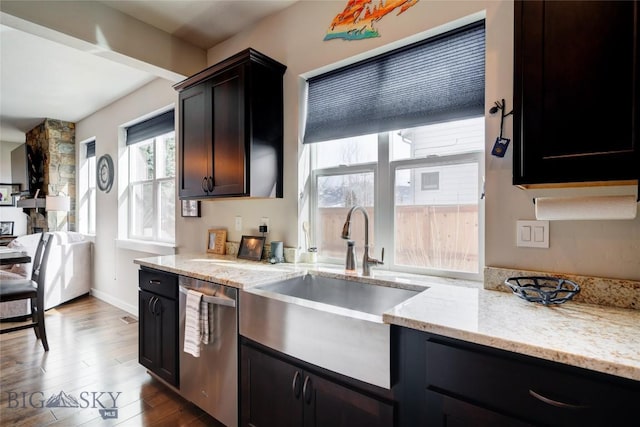 kitchen featuring dishwasher, dark wood-type flooring, light stone counters, and a sink