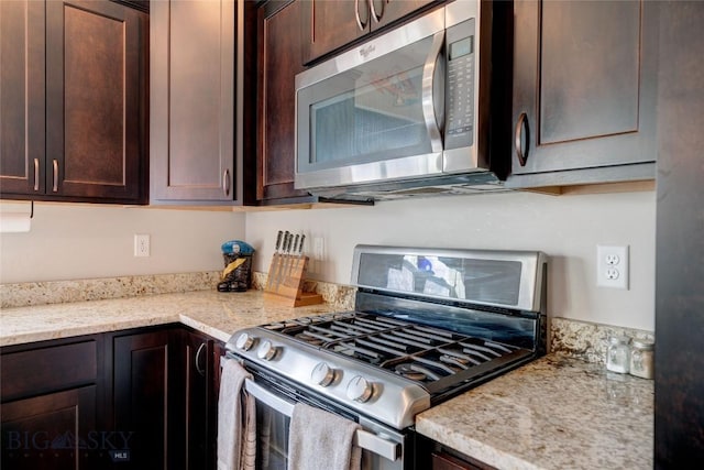 kitchen with dark brown cabinets, stainless steel appliances, and light stone countertops