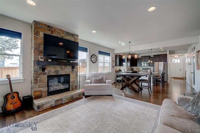 living room featuring a stone fireplace, recessed lighting, baseboards, and dark wood-style flooring