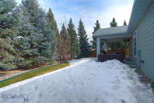 yard layered in snow with fence and a hot tub