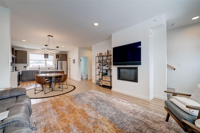 living area with recessed lighting, light wood-type flooring, and a glass covered fireplace