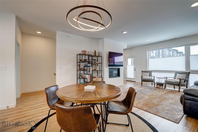 dining space with baseboards, light wood finished floors, recessed lighting, a glass covered fireplace, and a notable chandelier