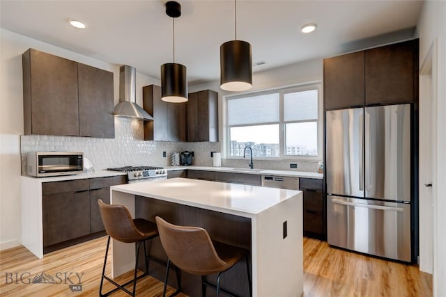 kitchen with a sink, stainless steel appliances, dark brown cabinets, wall chimney range hood, and light wood-type flooring