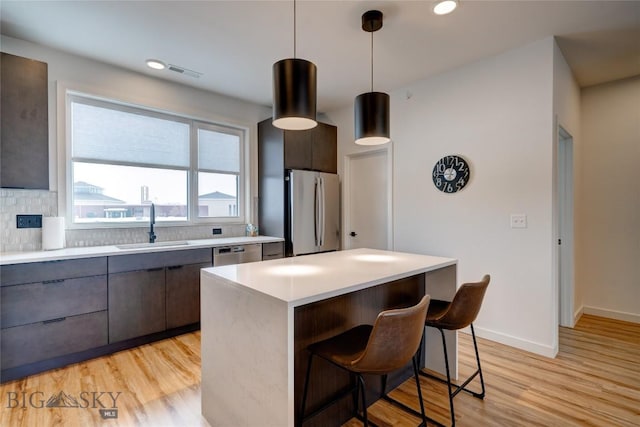 kitchen with light wood finished floors, light countertops, a kitchen breakfast bar, stainless steel appliances, and a sink