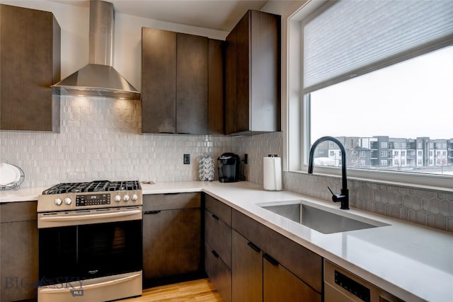 kitchen with gas range, light countertops, wall chimney range hood, and a sink