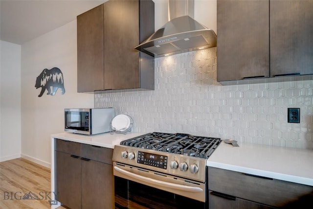 kitchen featuring light countertops, dark brown cabinets, appliances with stainless steel finishes, wall chimney exhaust hood, and tasteful backsplash