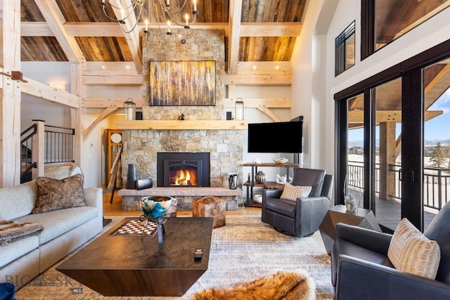 living room with beam ceiling, a stone fireplace, a high ceiling, and a notable chandelier