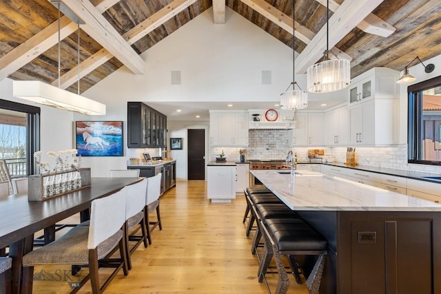 kitchen with beam ceiling, white cabinetry, light wood-style floors, decorative backsplash, and a large island with sink