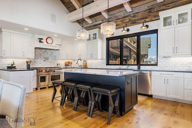 kitchen featuring stainless steel appliances, beamed ceiling, a breakfast bar area, and light wood-style flooring