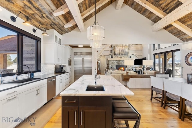 kitchen with light wood finished floors, a sink, decorative backsplash, wood ceiling, and appliances with stainless steel finishes