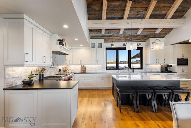 kitchen with a sink, light wood-style floors, appliances with stainless steel finishes, white cabinetry, and beamed ceiling