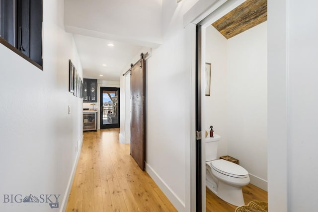 hallway featuring beverage cooler, recessed lighting, a barn door, light wood-style floors, and baseboards