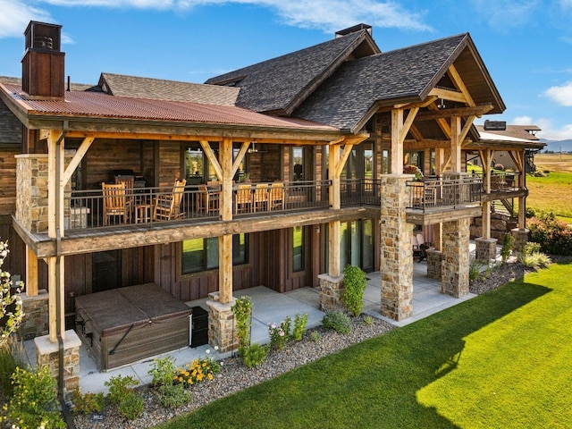 back of house with a lawn, a shingled roof, a balcony, a chimney, and a patio area