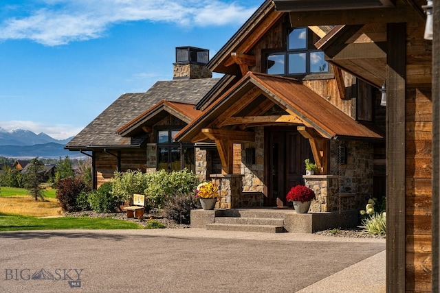 doorway to property featuring a mountain view, stone siding, and a shingled roof