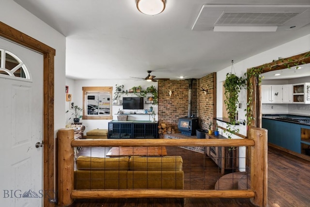 living room featuring a ceiling fan, a wood stove, wood finished floors, and visible vents