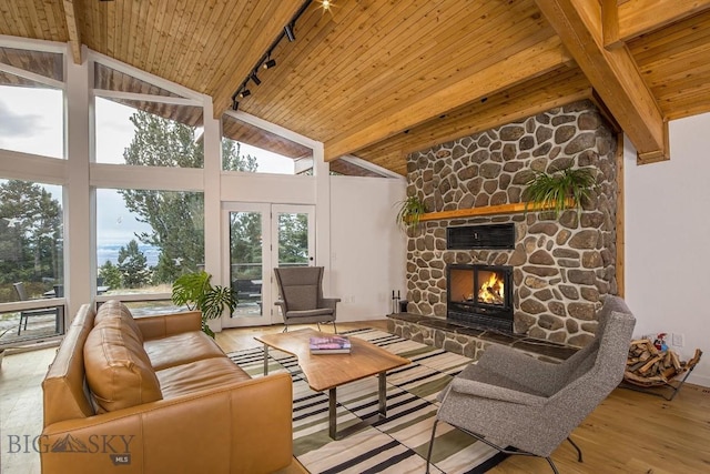 living area featuring beamed ceiling, high vaulted ceiling, wood finished floors, a stone fireplace, and wooden ceiling