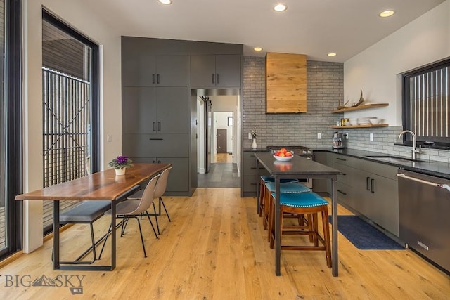 kitchen featuring dark countertops, tasteful backsplash, stainless steel dishwasher, light wood-style floors, and a sink