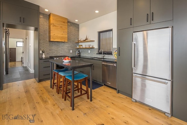 kitchen featuring light wood-style flooring, a sink, appliances with stainless steel finishes, dark countertops, and backsplash