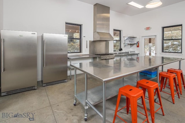 kitchen with freestanding refrigerator, stove, wall chimney exhaust hood, and stainless steel counters