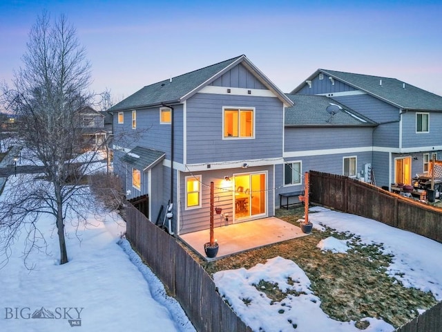 snow covered property featuring board and batten siding, a fenced backyard, and a patio