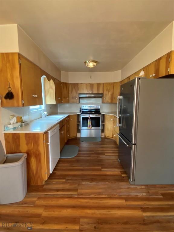 209 2nd St E, Whitehall, MT 59759 - kitchen featuring appliances with stainless steel finishes, under cabinet range hood, brown cabinetry, dark wood-style floors, and light countertops
