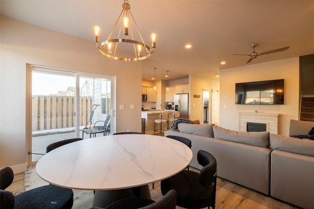 dining area with baseboards, light wood-type flooring, recessed lighting, a fireplace, and ceiling fan with notable chandelier