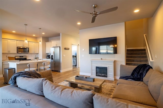 living room with a glass covered fireplace, stairs, light wood-style floors, and recessed lighting