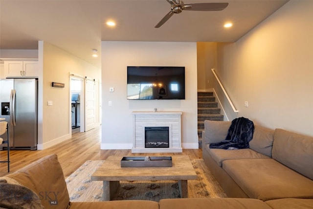 living room with light wood finished floors, recessed lighting, ceiling fan, stairs, and a barn door